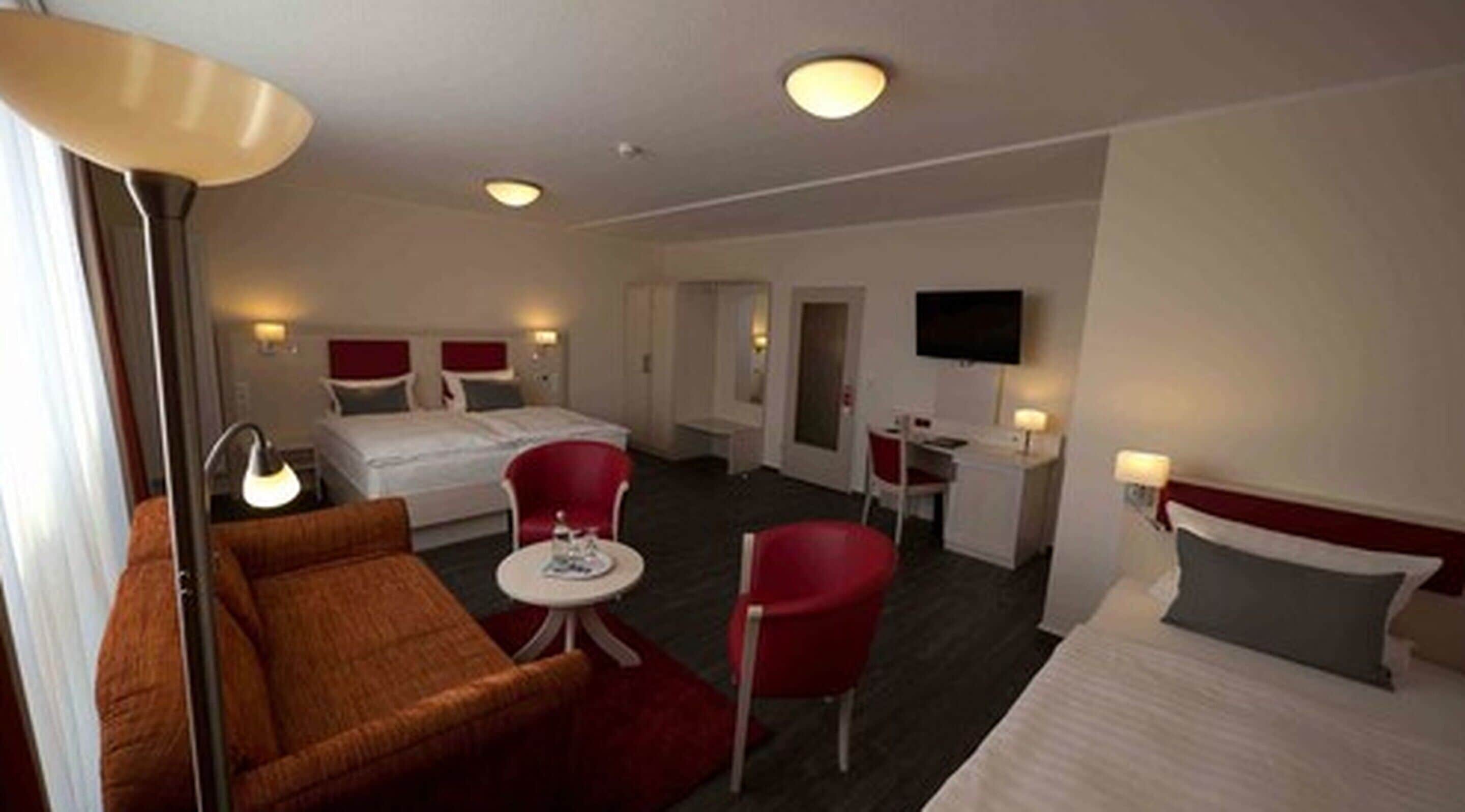 A hotel room with a bed, a sofa, a desk, and a TV.