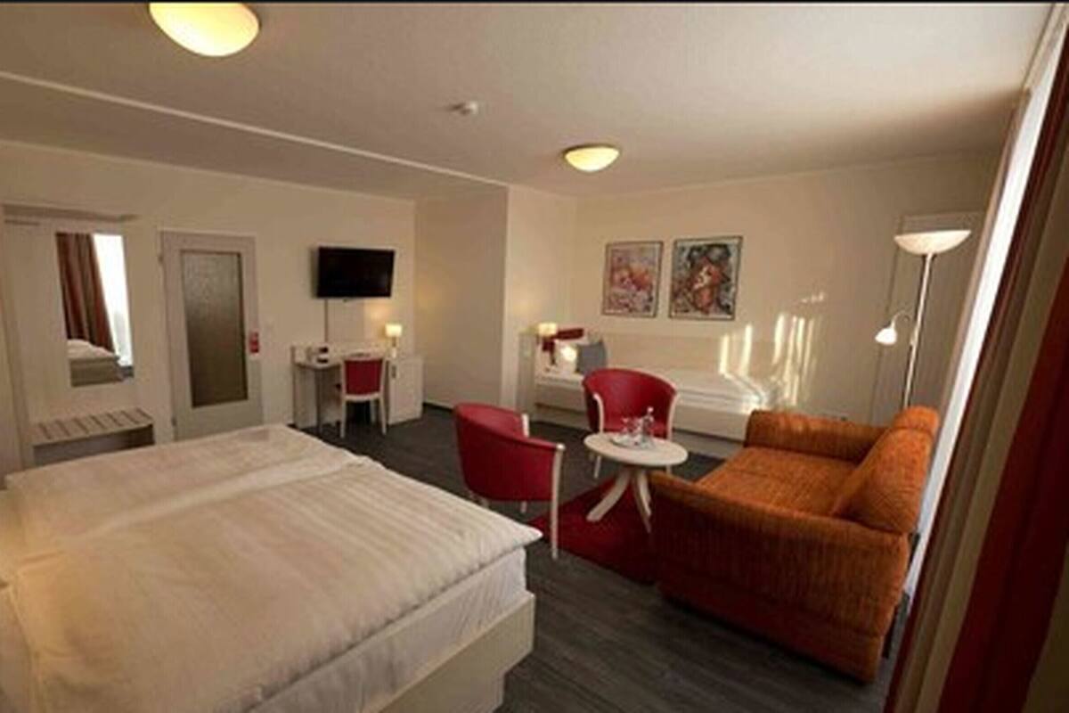 A hotel room with a bed, a red armchair, a small table, and a TV mounted on the wall.