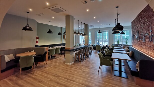 Ein modernes Restaurant mit hohen Decken, Holzböden und einer Mischung aus Sitzgelegenheiten, darunter Tische und Sitzecken.