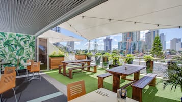 Una terraza en la azotea con mesas y sillas de madera, césped artificial verde y plantas en macetas.