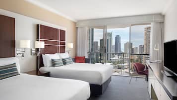 Une chambre d’hôtel avec deux lits, une télévision, un bureau et un balcon donnant sur la ville.