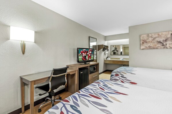 A hotel room with a bed, desk, chair, TV, and a small refrigerator.