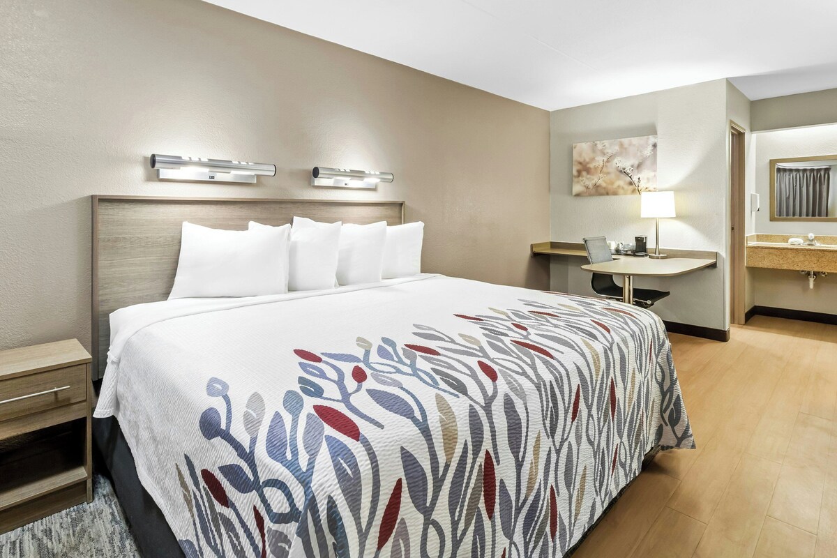 A hotel room with a bed, bedside table, lamp, and a bathroom with a sink and mirror.