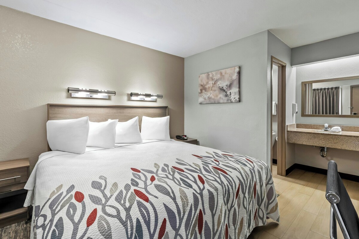 Une chambre d’hôtel comprenant un lit, une table de chevet, une commode et une salle de bain avec un miroir, un lavabo et un porte-serviettes.