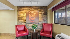 A Red Roof Inn lobby with a stone wall, two red leather chairs, a small table with a plant, and a large window. - Red Roof Inn Dayton North Airport (Dayton)