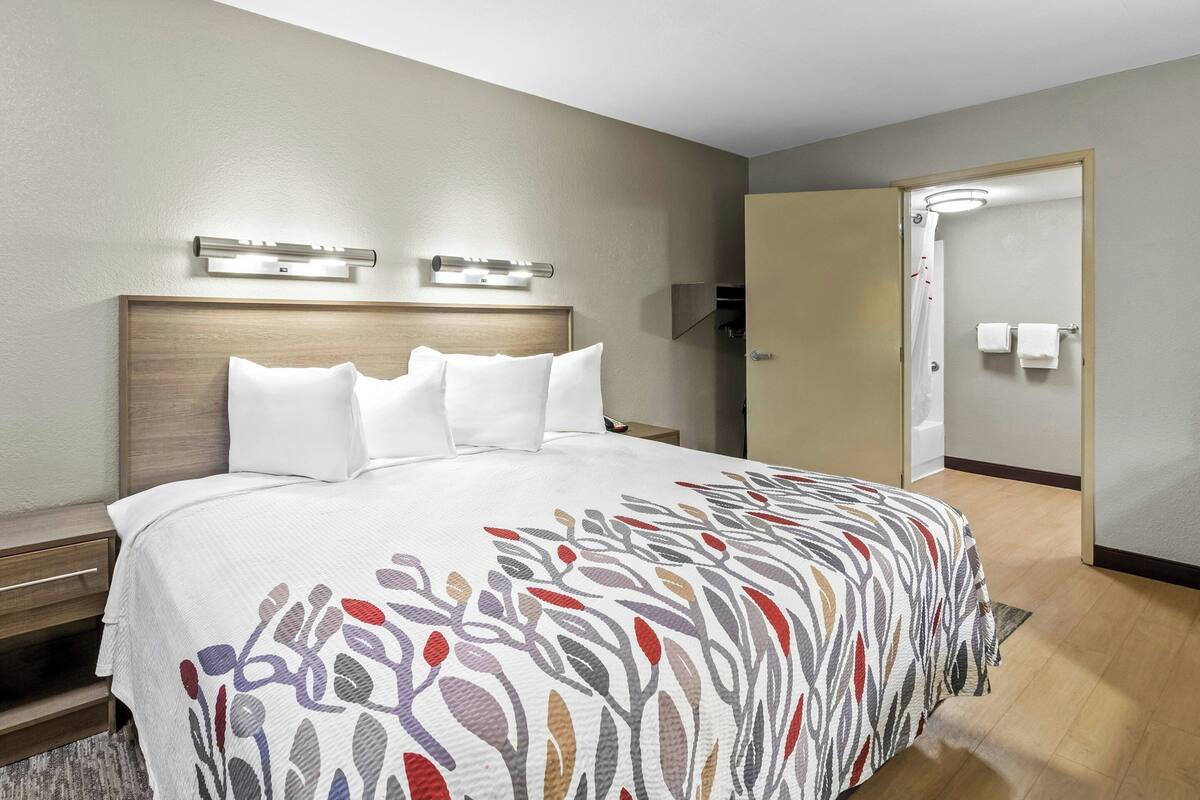 Habitación de hotel con cama, mesitas de noche, cabecera, zona de ducha y una puerta.