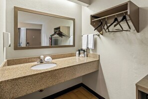 A bathroom with a granite countertop sink, a mirror, a towel rack, and a wooden shelf. - Red Roof Inn Dayton North Airport (Dayton)