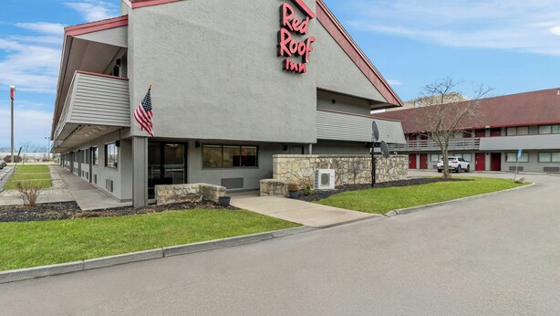 A Red Roof Inn with a modern design, a stone facade, and an American flag. - Red Roof Inn Dayton North Airport (Dayton)