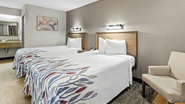 A hotel room with two beds, a chair, a mirror, and a wall-mounted light fixture. - Red Roof Inn Dayton North Airport (Dayton)