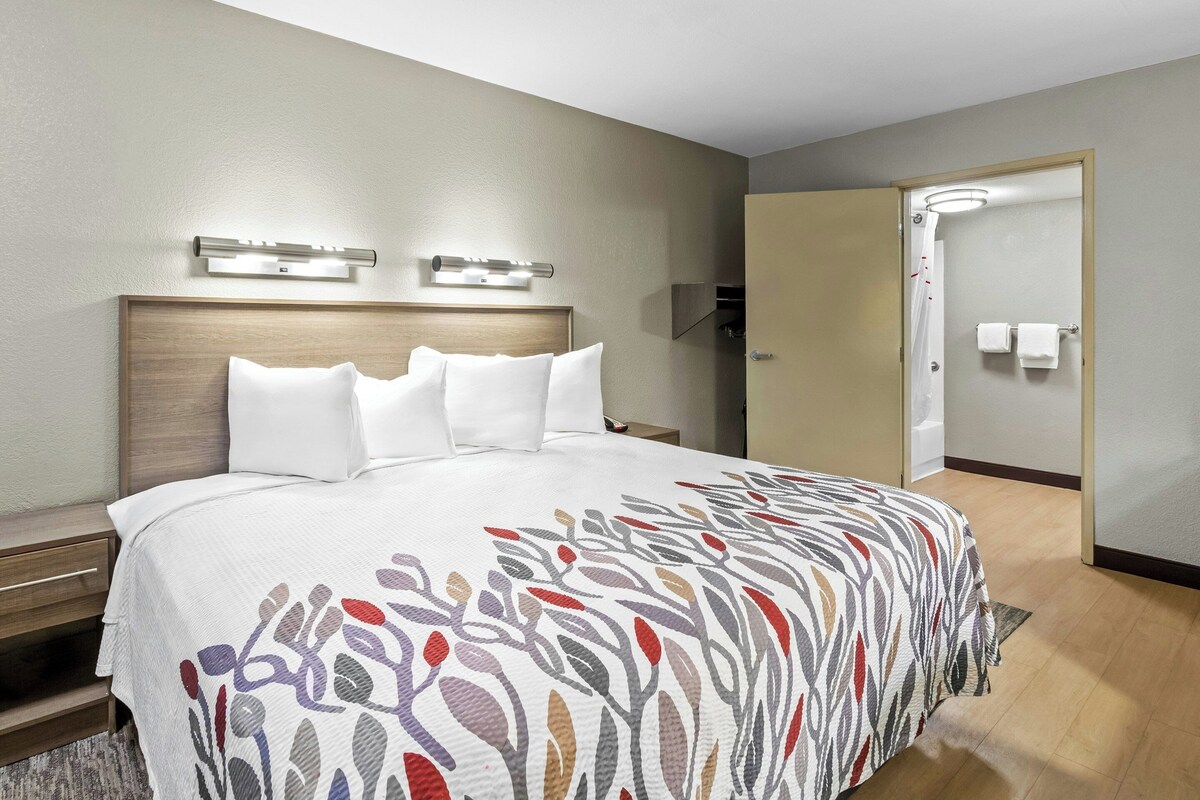 A hotel room with a bed, bedside tables, a headboard, a shower area, and a door.