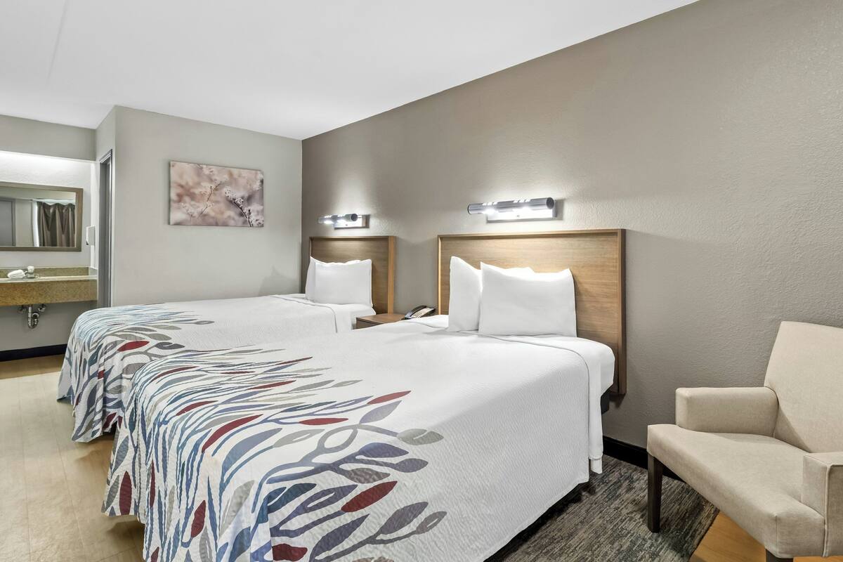 Una habitación de hotel con dos camas, una silla, un espejo y una lámpara fijada a la pared.