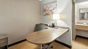 A hotel room with a conference table, a chair, a lamp, a coffee maker, a sink, and a mirror. - Red Roof Inn Dayton North Airport (Dayton)