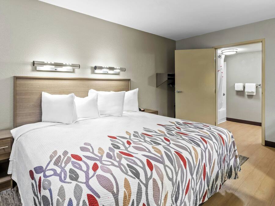 A hotel room with a bed, bedside tables, a headboard, a shower area, and a door.