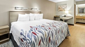 A hotel room with a bed, bedside table, lamp, and a bathroom with a sink and mirror. - Red Roof Inn Dayton North Airport (Dayton)