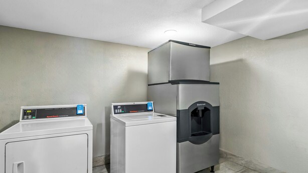 A laundry room with a front-loading washer, a top-loading dryer, and a water dispenser. - Red Roof Inn Dayton North Airport (Dayton)