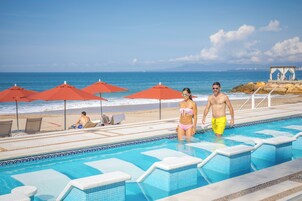 Zona de piscina con vista al océano, sombrillas rojas y sillas de descanso.