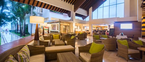 A spacious lobby with wicker furniture, a pool view, and a bar area.