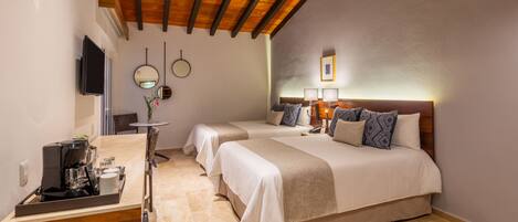A hotel room with two beds, a coffee station, a TV, and a ceiling with exposed beams.