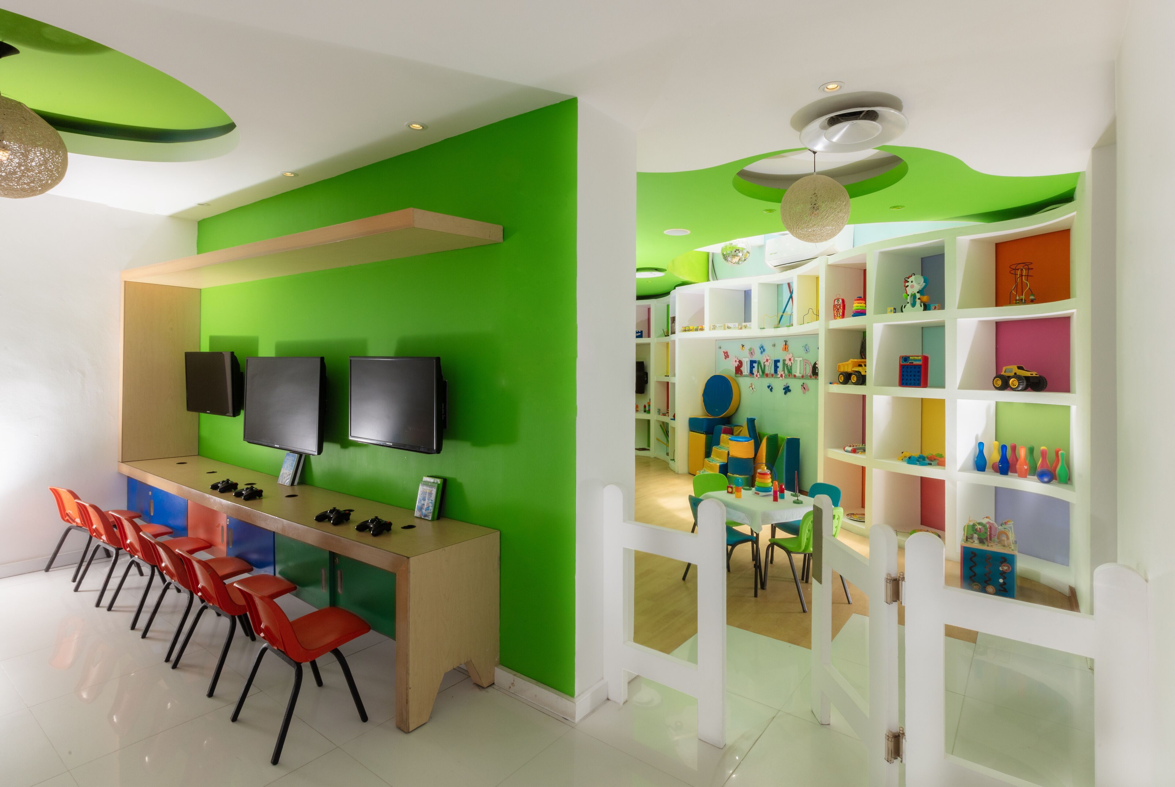 Une salle de jeux moderne pour enfants, avec un mur vert, un téléviseur et un espace de jeu doté d’étagères colorées.