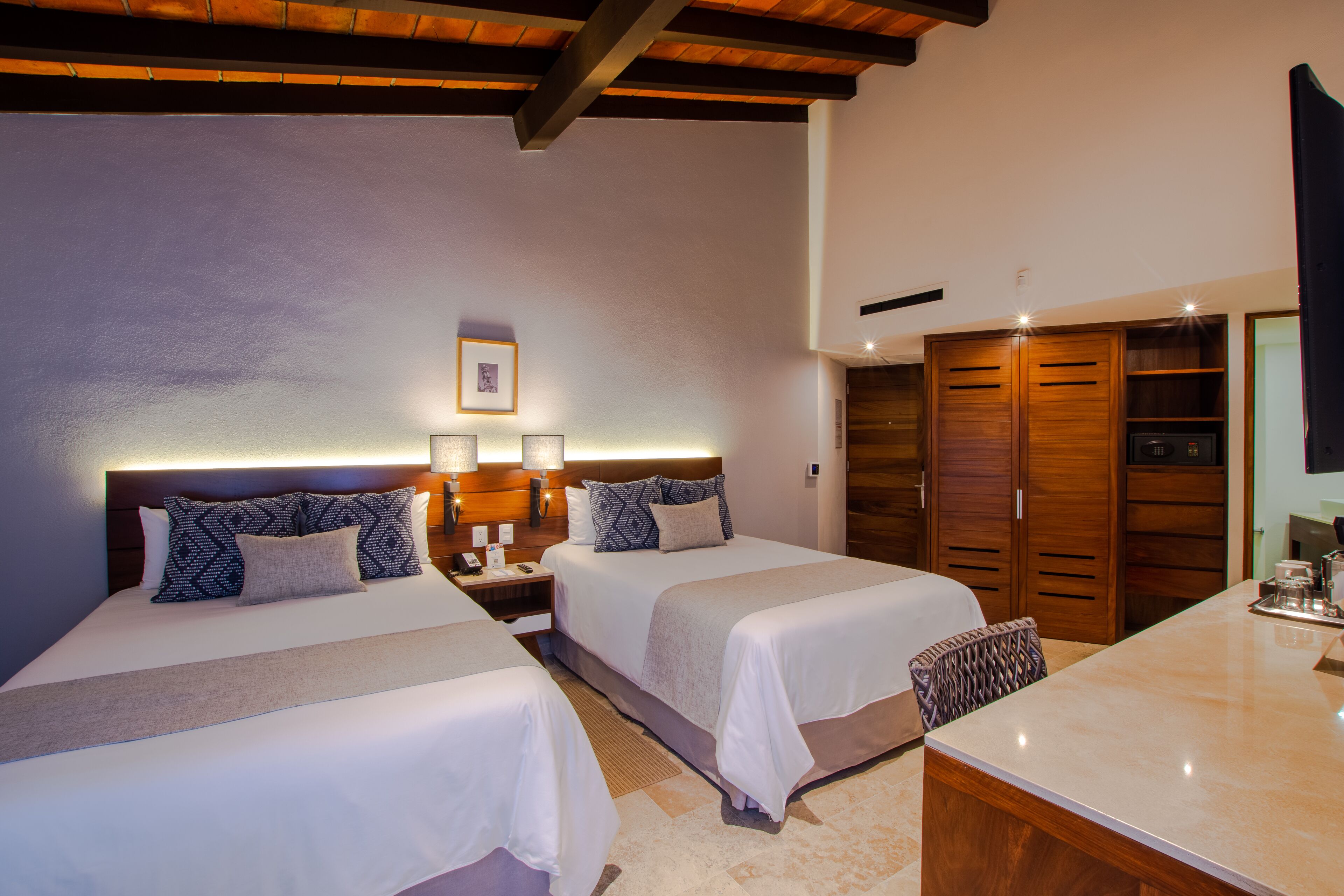 A hotel room with two beds, a desk, a wardrobe, and a nightstand with a lamp.
