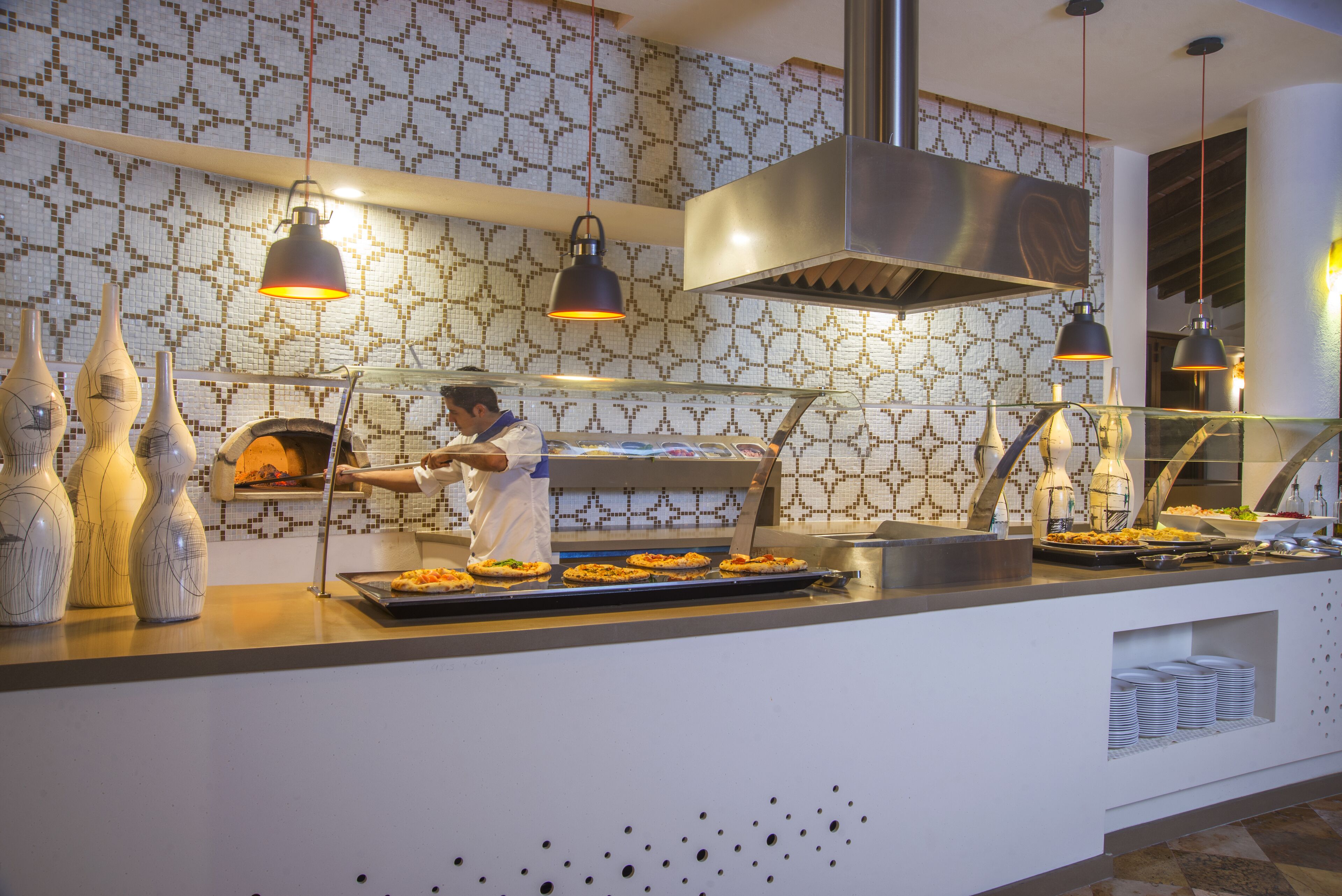 Een buffetopstelling met een kok die eten bereidt, een pizzaoven en decoratieve vazen.