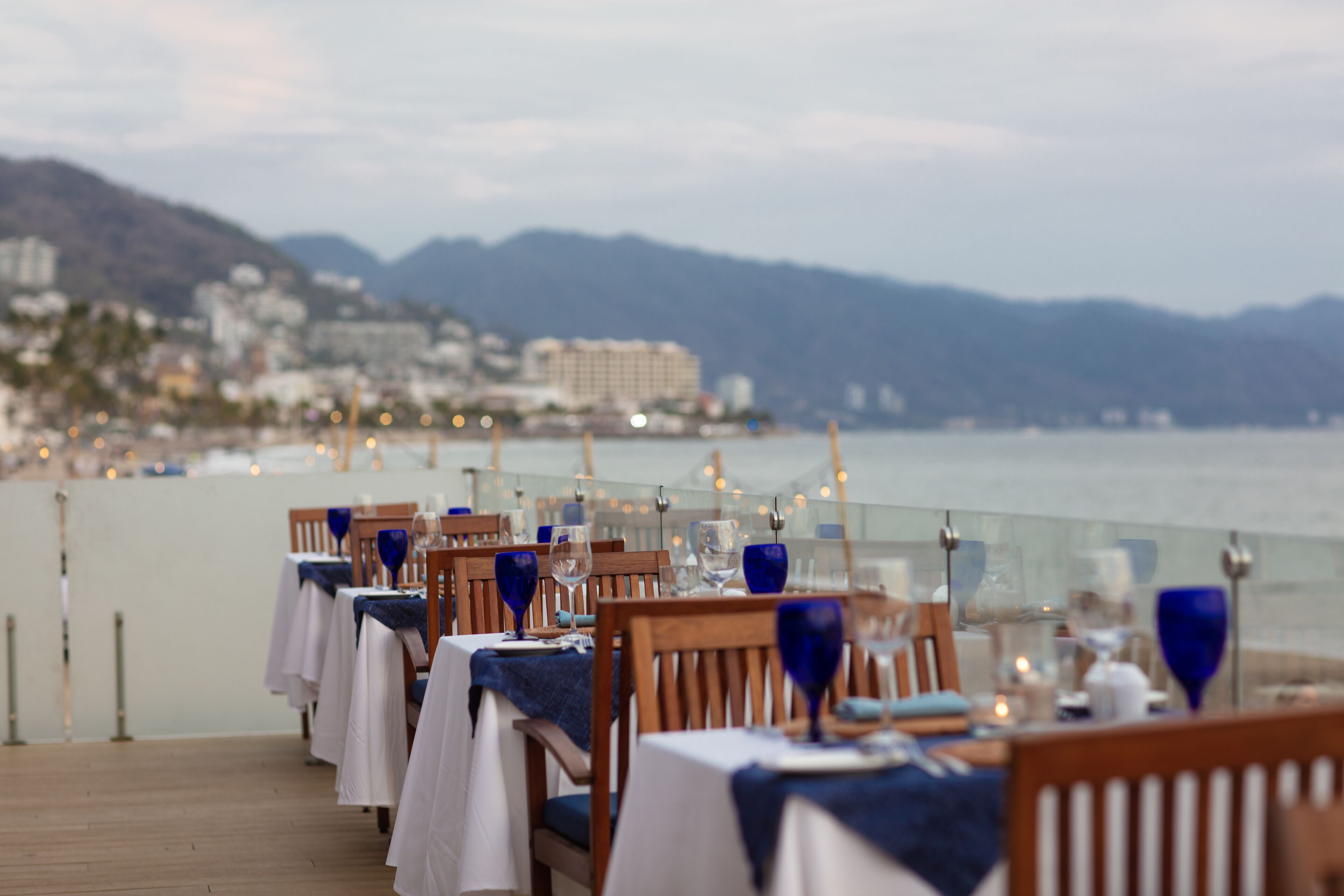A dining area with tables set for a meal, overlooking a body of water and a mountainous landscape.