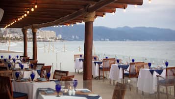 An outdoor dining area with tables set for a meal, overlooking a beach and the sea.