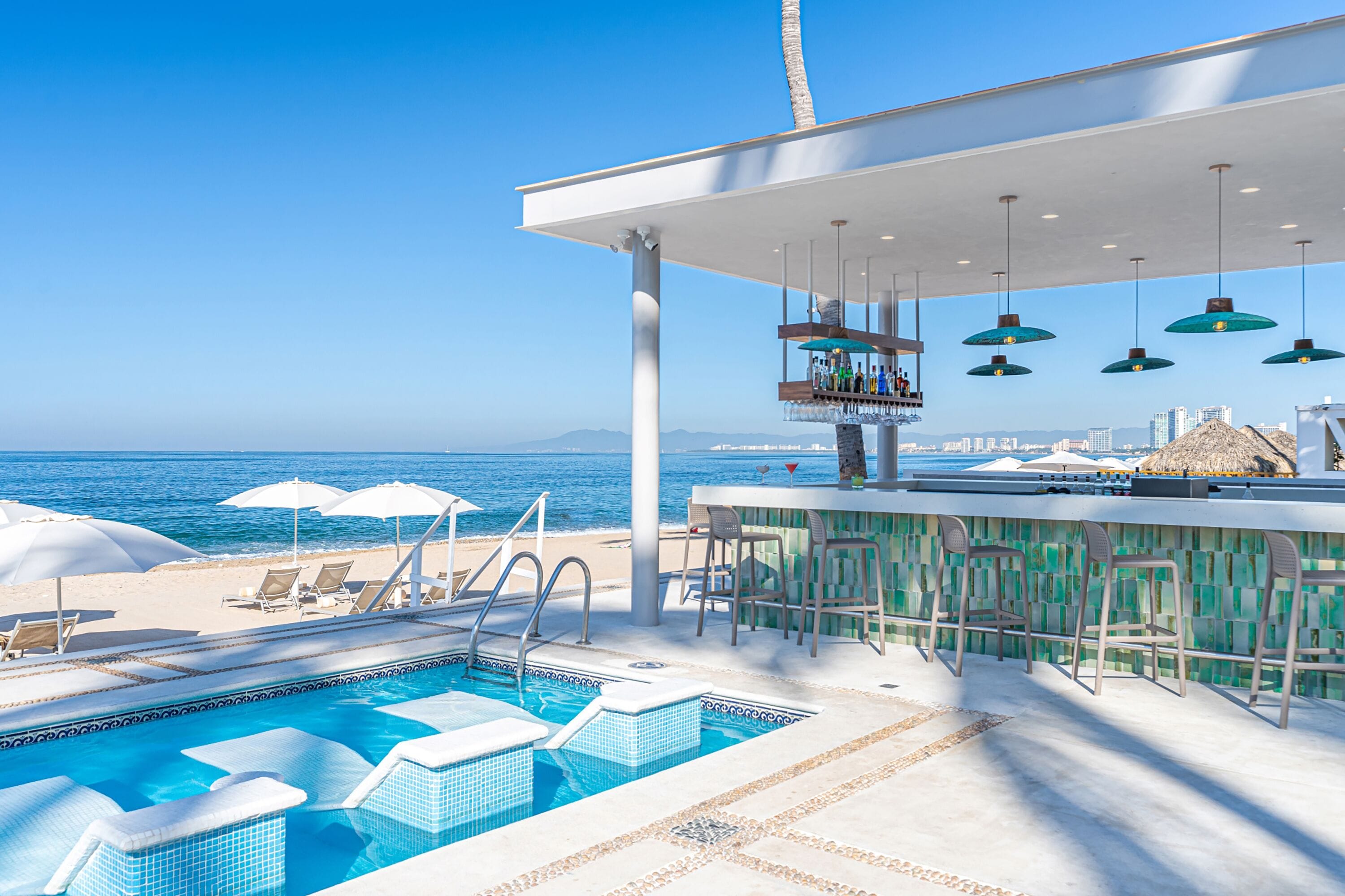 A poolside bar with a view of the ocean, lounge chairs, and umbrellas.