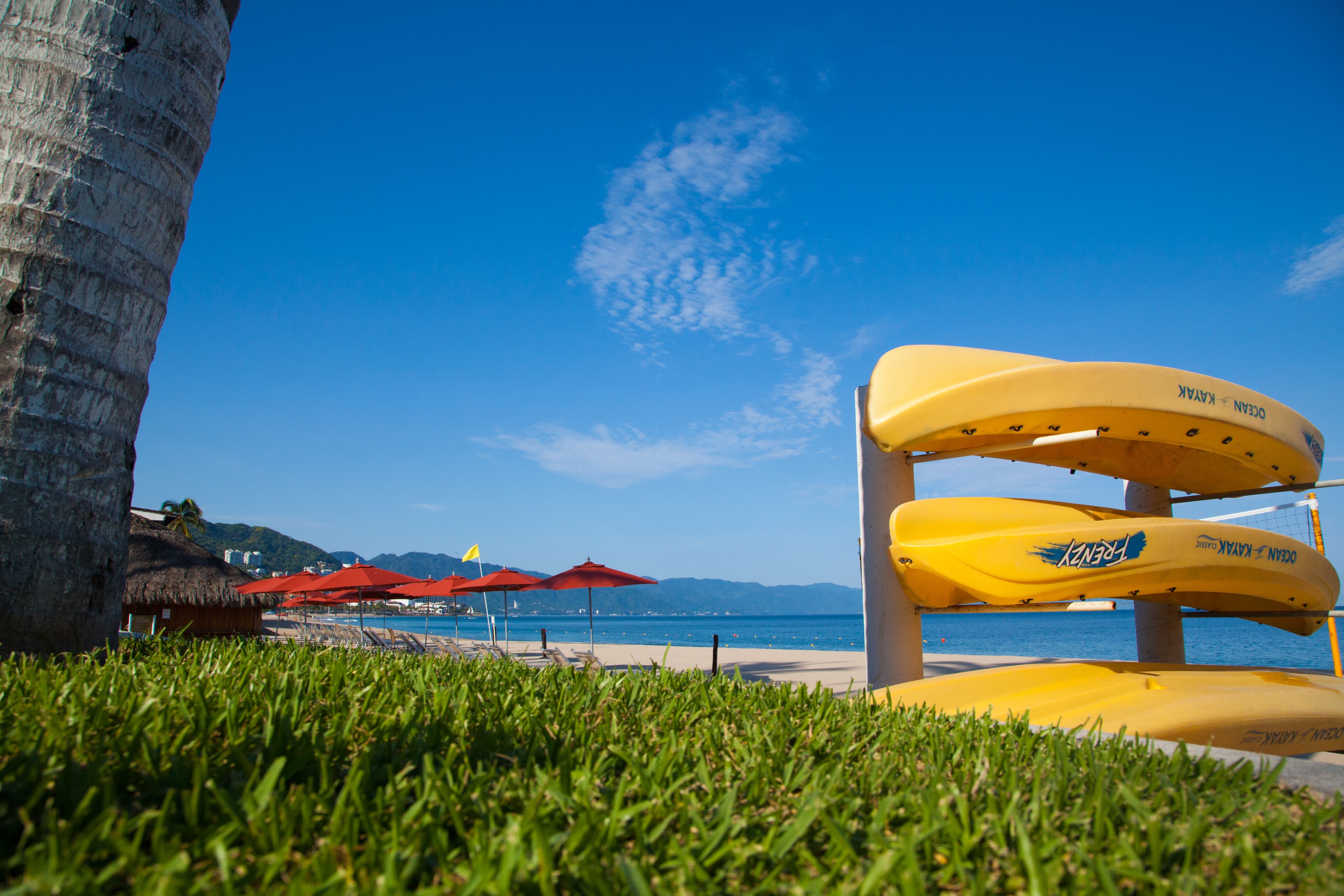 Une scène de plage avec une chaise de sauveteur, des parasols rouges et un abri à toit de chaume.