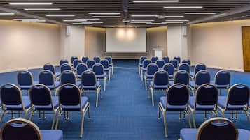 Un salón de conferencias con filas de sillas orientadas hacia una pantalla grande y un atril.