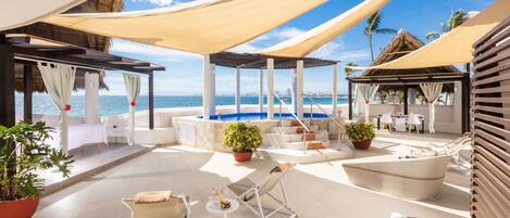 A beachside lounge with a pool, outdoor seating, and potted plants.