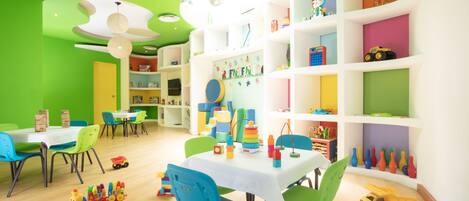 A brightly colored children's playroom with a white table, blue chairs, and shelves filled with toys.