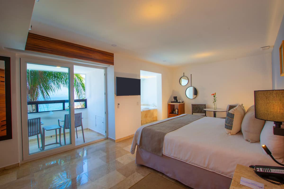 Une chambre avec un grand lit, un bureau, une chaise, une télévision et un balcon équipé de chaises.