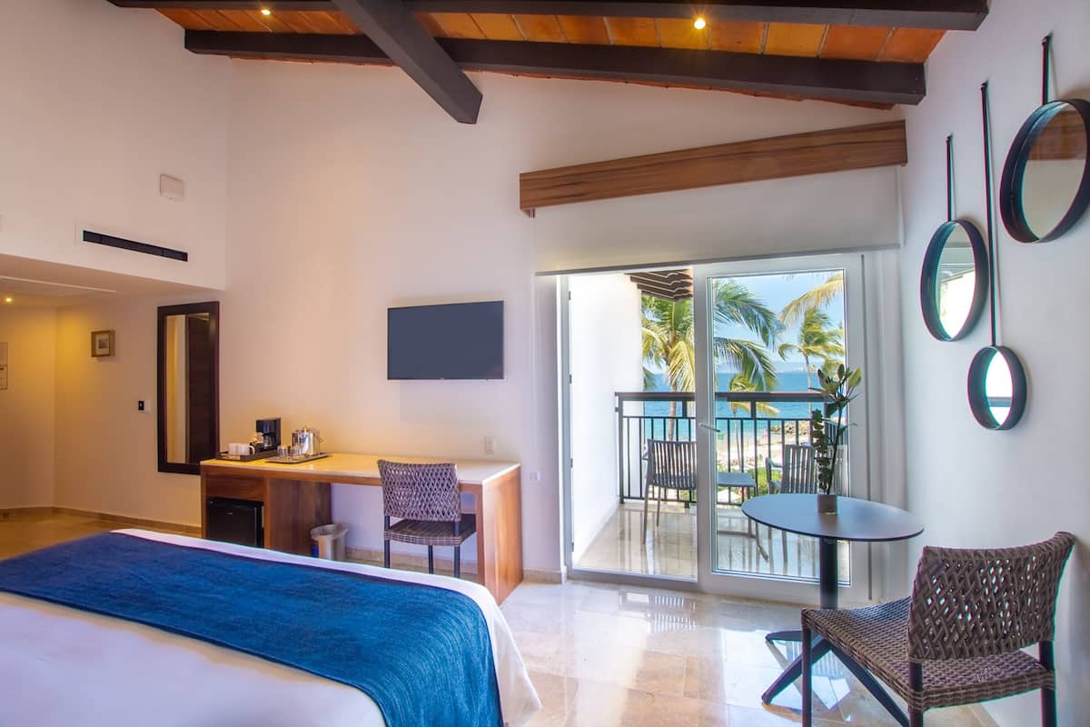 Une chambre d’hôtel équipée d’un lit, d’un bureau, d’une chaise et d’un balcon offrant une vue sur les palmiers.