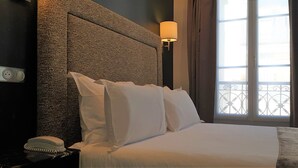Habitación de hotel con una cama grande, cabecero, lámpara de noche, teléfono y ventana con cortinas.