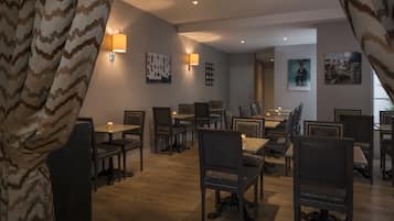Un comedor con varias mesas y sillas, luminarias fijadas a la pared y obras de arte enmarcadas.