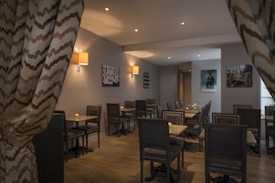 Una sala da pranzo con diversi tavoli e sedie, lampade a parete e quadri appesi alle pareti.