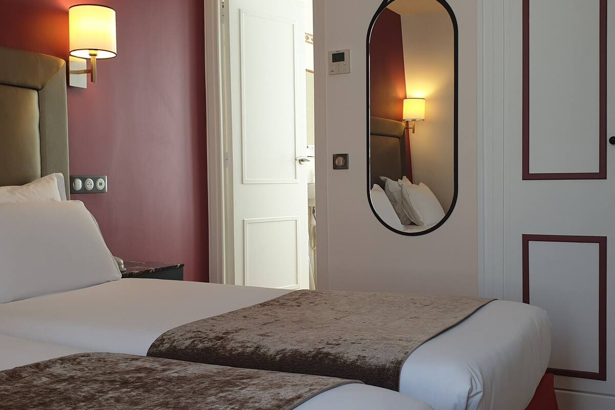 Quarto de hotel com cama, luminárias de cabeceira, guarda-roupa e espelho.