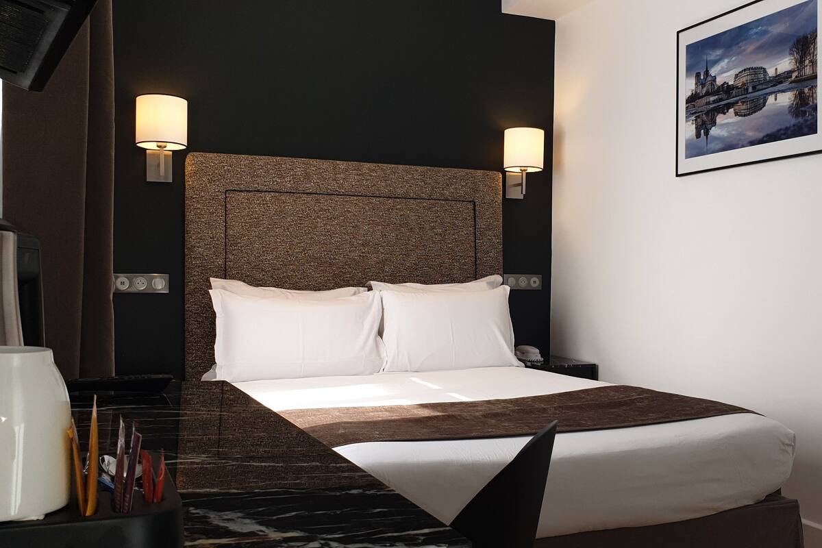 Quarto de hotel com uma cama grande, duas luminárias de cabeceira, uma cafeteira e um quadro na parede.