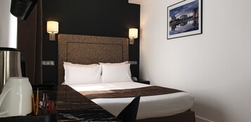 A hotel room with a large bed, two bedside lamps, a coffee maker, and a framed picture on the wall.