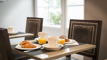 A breakfast setting with croissants, orange juice, and coffee on a table with chairs.