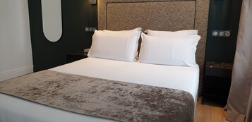 A neatly made bed with white linens and a brown throw blanket, a textured headboard, and a small bedside table with a lamp.