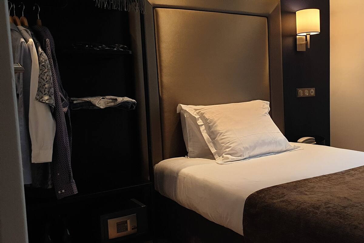 Quarto de hotel com cama, guarda-roupa e mesa de cabeceira.