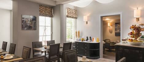 A dining area with tables and chairs, a bar area with a fruit bowl, and a view of the outdoors through large windows.
