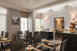 A dining area with tables and chairs, a bar area with a fruit bowl, and a view of the outdoors through large windows.