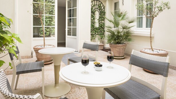 Un patio con mesas y sillas redondas, plantas en macetas y vistas al jardín.