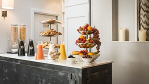 Un bufé de desayuno con diversas frutas, pasteles y bebidas sobre una encimera de mármol.
