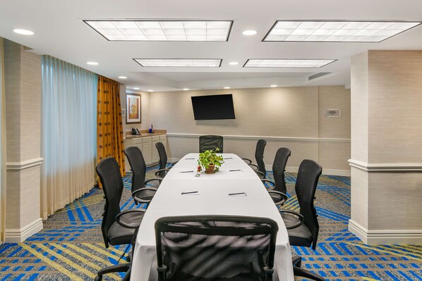 A conference room with a long table, black chairs, a plant, and a flat-screen TV on the wall. - DoubleTree by Hilton Hotel Jefferson City (Jefferson City)