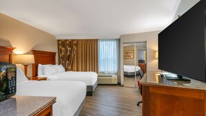 Ett hotellrum med två sängar, en tv, ett skrivbord med en telefon och en spegel.