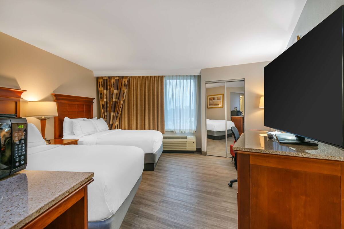 Ein Hotelzimmer mit zwei Betten, einem Fernseher, einem Schreibtisch mit Telefon und einem Spiegel.